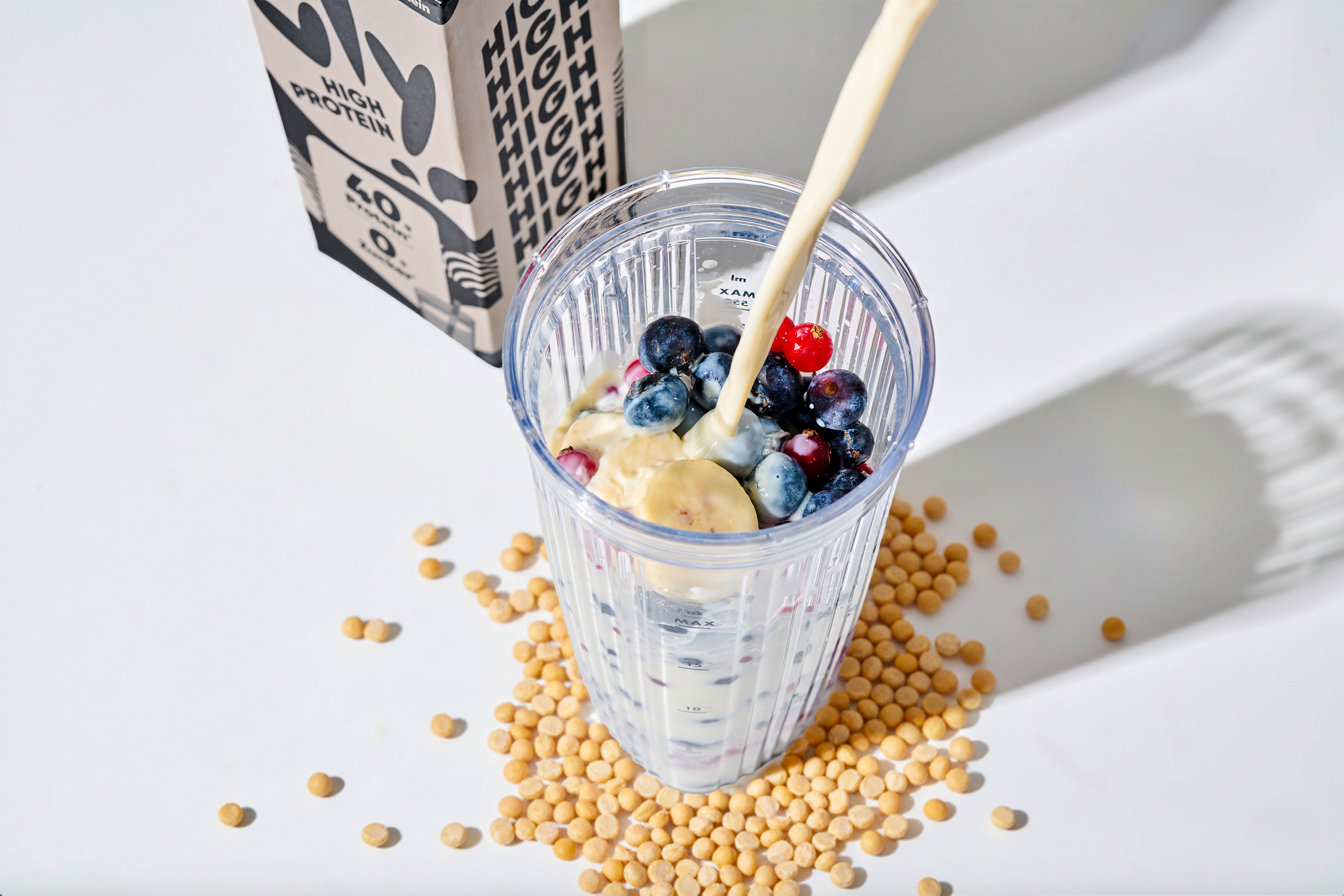 glass of pea milk on a table with peas lying on the table and the package in the background
